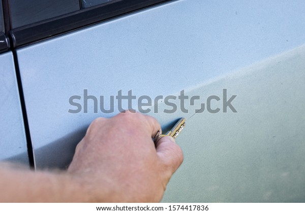 male hand scratches\
car wing with a key