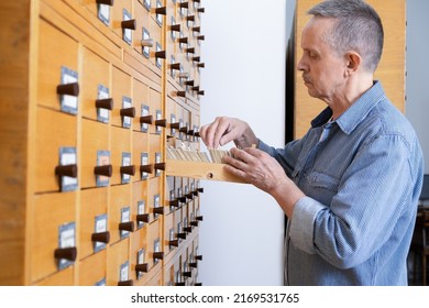 A male hand searching cards in old wooden card catalogue. A vintage library catalogue, for a convenient and quick search for a book. Man searching file in the library card index