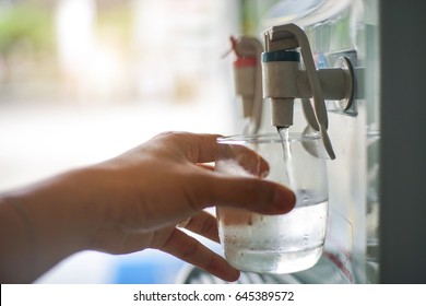 Male hand serving water of a water cooler in plastic cup.
				