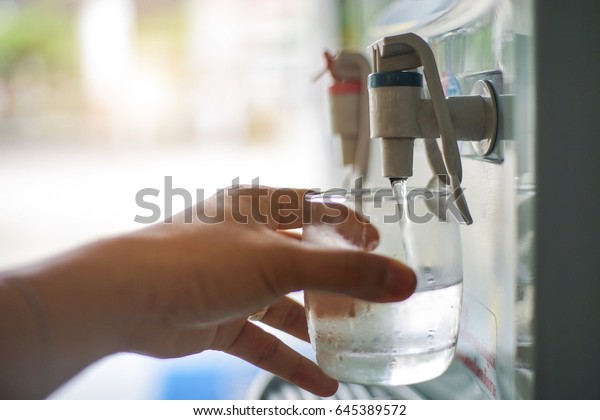 Male hand serving water of a water cooler in\
plastic cup.\
