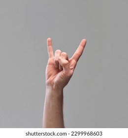 Male hand showing gesture of rock and roll, Hook 'Em Horns against grey background. Having good time signal. Youth communication. Concept of human relation, community, symbolism, culture - Powered by Shutterstock