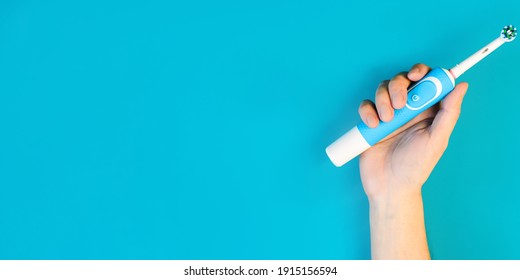 Male Hand Showing Modern Electric Toothbrush On Blue Background. Banner With Empty Place For Text. Controlled Oral Hygiene Tool, Ad Space.