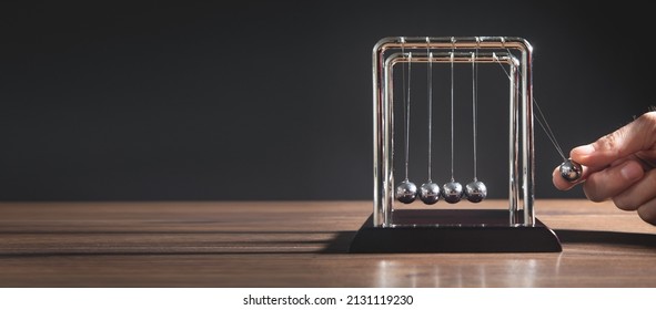 Male hand showing Newton's cradle balls on the wooden table. Business - Shutterstock ID 2131119230