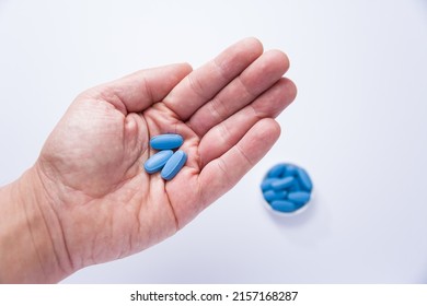 Male hand showing three pills in the palm and in the background out of focus a container full of blue tablets