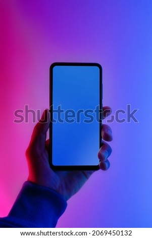 Male hand with smartphone. Neon illumination. Pink and blue color. Flat screen smartphone