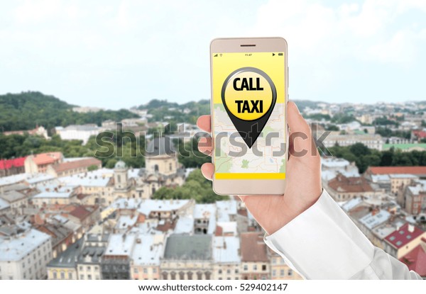 Male hand with smartphone on\
cityscape background. Taxi service application on\
screen.