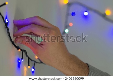 male hand sticking christmas string lights on a wall with tape, decorating home with christmas lights close up