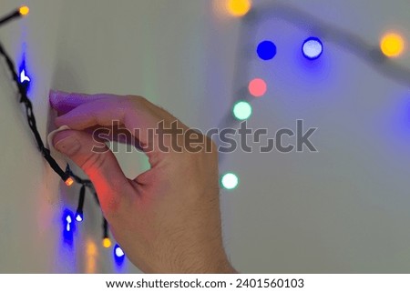 male hand sticking christmas string lights on a wall with tape, decorating home with christmas lights close up