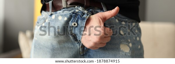 Male hand sticking out of fly of his jeans and\
showing thumb up close-up. Treatment of sexual dysfunction in men\
concept