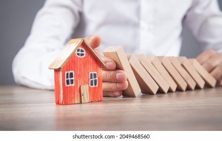 Male Hand Stopping Wooden Blocks On House.