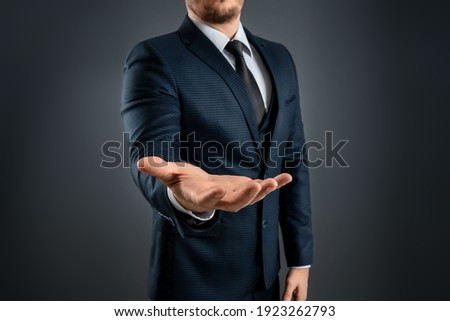 Male hand in a suit shows a palm up gesture on a gray background. Concept of request, bankruptcy, close-up