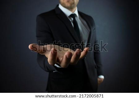 Male hand in a suit shows a palm up gesture on a black background. Concept of request, bankruptcy, close-up.