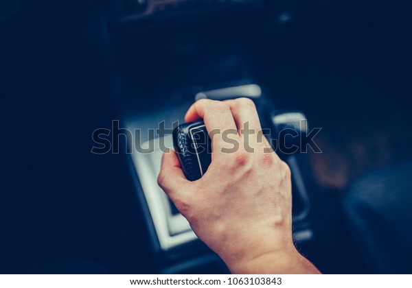 Male hand switches the automatic transmission\
close-up. Close-up of the driver\'s arm includes mode Drive on the\
gear lever automatic transmission of the luxury car. Stylish Toned\
Photo Top view