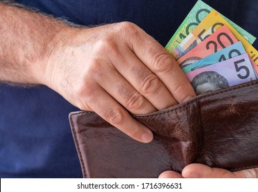 Male hand taking Australian bank notes from a worn brown wallet.  Financial