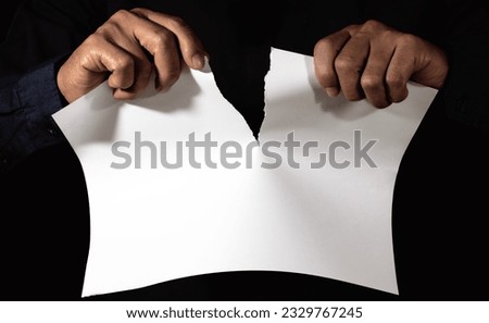 Male hand tearing paper close up on a dark background
