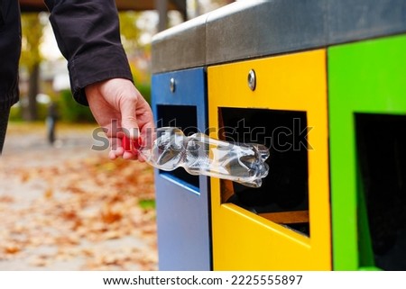 Male hand throwing a plastic bottle into a yellow garbage bin in the local park. Responsible waste sorting, collection and recycling concept.