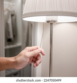 Male hand turn off the light on torchiere lamp in bedroom. Saving electricity energy at night. Switch off lighting equipment for bedtime. - Shutterstock ID 2247050499