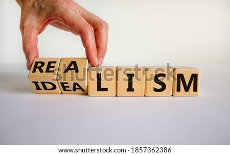 Male hand turns cubes and changes the expression 'idealism' to 'realism' or vice versa. Beautiful white background. Business concept. Copy space.