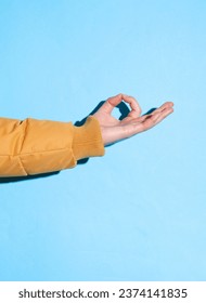 Male hand in a warm winter jacket showing zen cymbol on a blue background