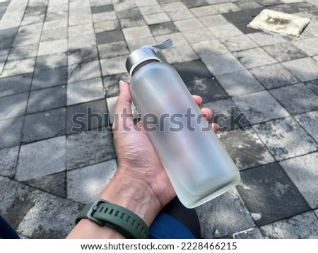 A male hand wearing watch holding a glass tumblr in a park.