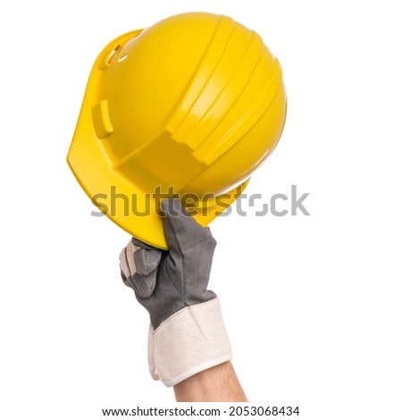 Male hand wearing working glove holding yellow hard hat. Close up of gloved hand of repairman with construction helmet, isolated on white background.