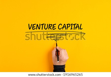 Male hand writing the business term venture capital on yellow background.
