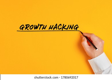 Male hand is writing the concept of growth hacking on yellow background. Growth hacking implies a massive growth in a short time on a small budget in business marketing.
