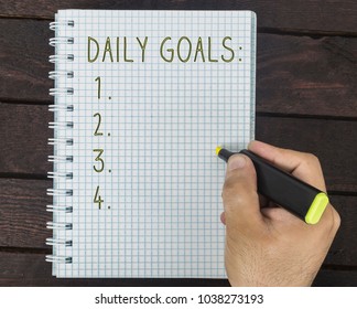 Male Hand Is Writing Daily Goals On A Notepad