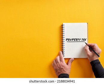 Male Hand Writing Property Tax On A Notepad.