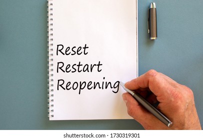 Male Hand Writing 'reset, Restart, Reopening' On White Note, Isolated On Blue Background.