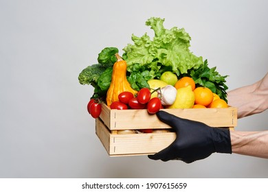 Male hands in black protective gloves hold a box with groceries. Online food delivery concept during quarantine. Fresh vegetables, fruits, food in a wooden box. Delivery from supermarket, farmers - Shutterstock ID 1907615659