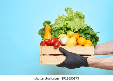 Male hands in black protective gloves hold a box with groceries. Online food delivery concept during quarantine. Fresh vegetables, fruits, food in a wooden box. Delivery from supermarket, farmers