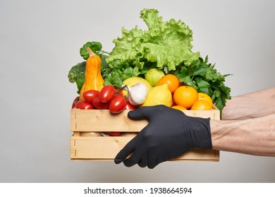 Male Hands In Black Protective Gloves Hold A Box With Groceries. Online Food Delivery Concept During Quarantine. Fresh Vegetables, Fruits, Food In A Wooden Box. Delivery From Supermarket, Farmers