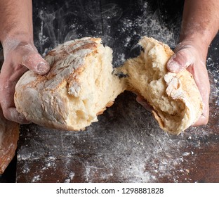 male hands breaking open baked bread in half over black wooden table - Powered by Shutterstock