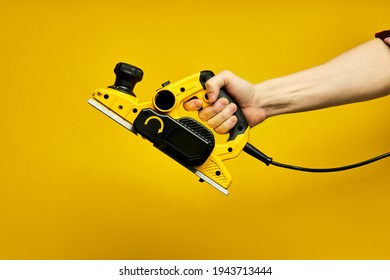 Male Hands Carpenter Holding Working Woodworking Power Tool In Hands, On Yellow Background