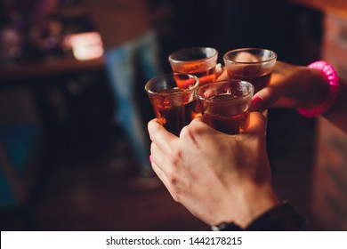 Male hands cheer with glasses of shot or liqueur. Friends drink shot or liqueur and cheers. Male hands cheer with alcohol on blurred bar background. Party and toast concept.