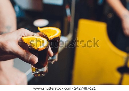 Male hands cheer with glasses of shot or liqueur. Friends drink shot or liqueur and cheers. Male hands cheer with alcohol on blurred bar background. Party and toast concept