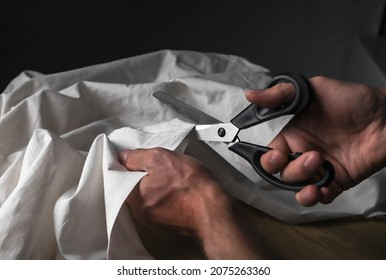 Male hands closeup cutting beige cotton or linen cloth with sewing scissors.