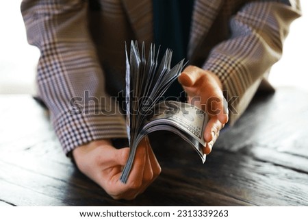 Male hands counting American one hundred dollar bills against the background of smaller bills of money lying on the table