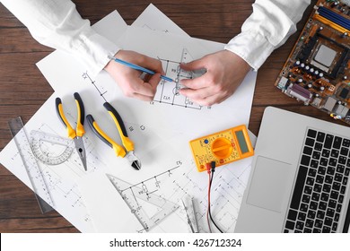 Male hands drawing electrical blueprint at wooden table, top view