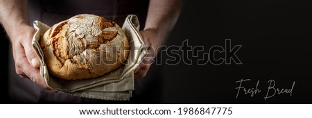 Male hands with fresh baked loaf rye wheat bread on a cotton towel. Dark background banner wirh copy space and text Fresh Bread
