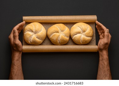 Male hands with fresh delicious kaiser rolls on baking paper against black background - Powered by Shutterstock