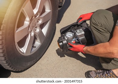 Male hands in glove and portable tire pump for inflating auto wheel. Tyre inflator air compressor with pressure gauge.