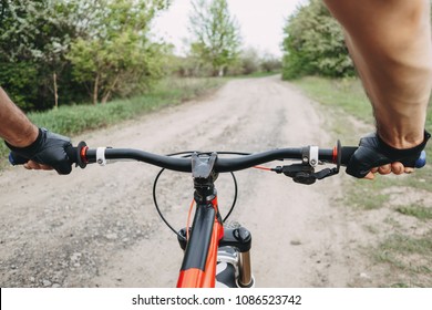 Male Hands In Gloves Holding Bicycle Handlebar. Riding A Bike First Person Perspective. Sports, Tourism And Activity Concept