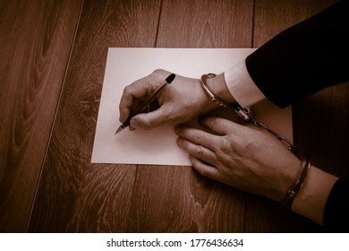 Male Hands In Handcuffs Hold A Pen In Front Of A Blank Sheet Of Paper. Concept Of A Detainee Signs A Document, Guilty Plea. Selective Focus. Blurred Background