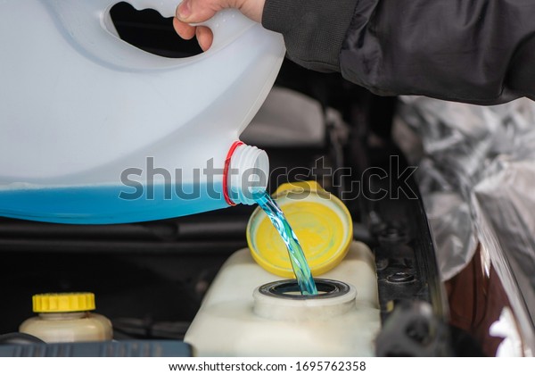 Male hands hold bottle of blue\
antifreeze, Pouring antifreeze liquid screen wash. man refills\
windshield wiper water on a car, Filling a windshield washer\
tank