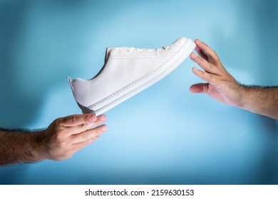 Male Hands Holding A Brand New Unbranded Stylish White Sneakers Or Tennis Shoes Over Blue Background