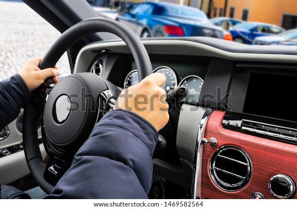 Male hands holding car steering wheel. Hands on\
steering wheel of a car driving. Young Man driving inside cabin.\
Multimedia system. Man Traveling In Self Driving Car. Car inside.\
Driving concept