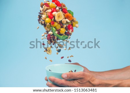 Male hands holding an empty blue bowl on blue background. Candied fruits and nuts flying above the bowl. Stock photo of nutrient and healty food. Conceptual photo of vegan and vegetarial food and meal
