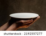 Male hands holding empty plate on dark background, lack of food, hunger and crisis concept
